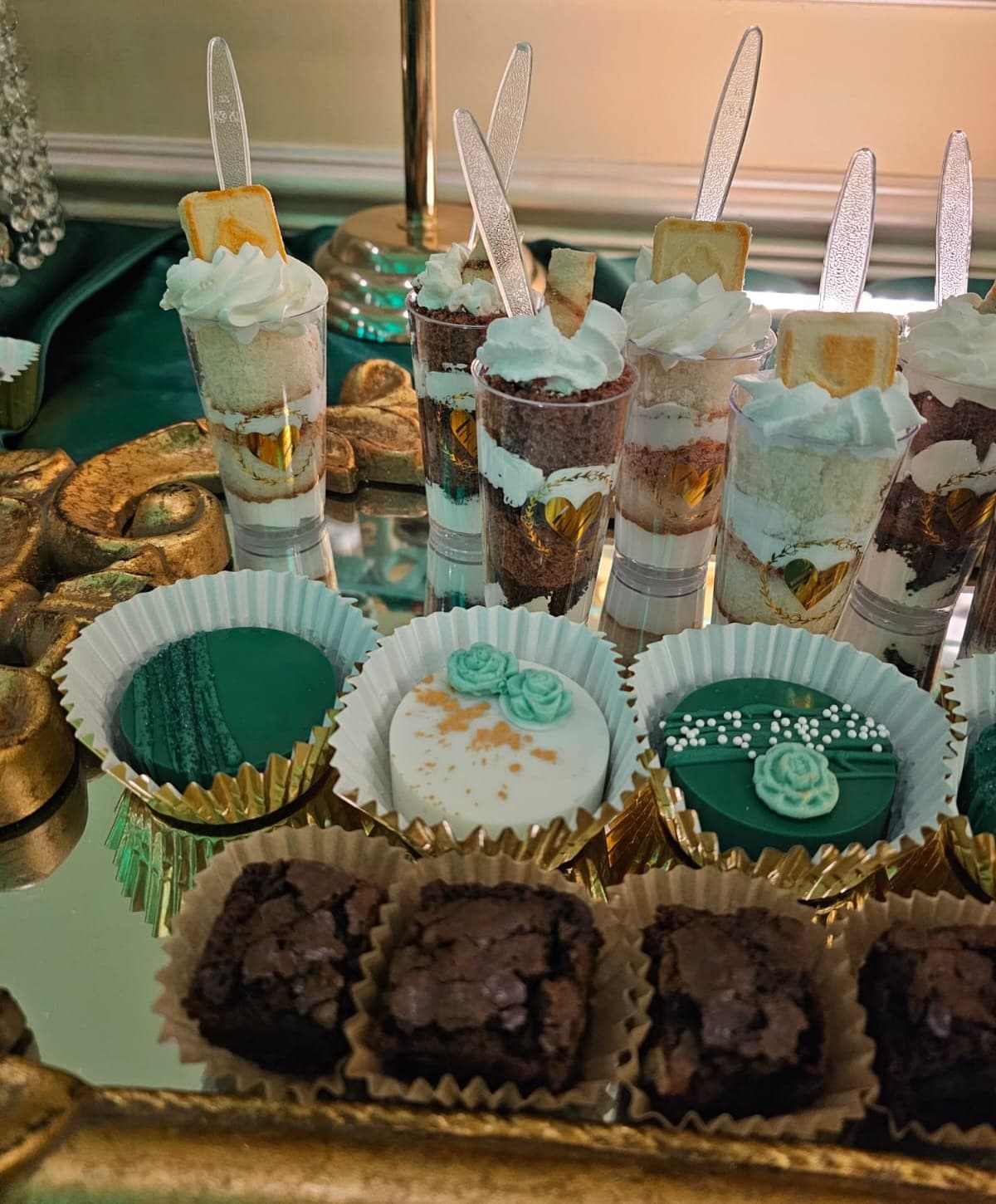 Layered vanilla and chocolate dessert cups with whipped cream, emerald and white chocolate-dipped Oreos with sugar roses, and brownies on a gold tray.
