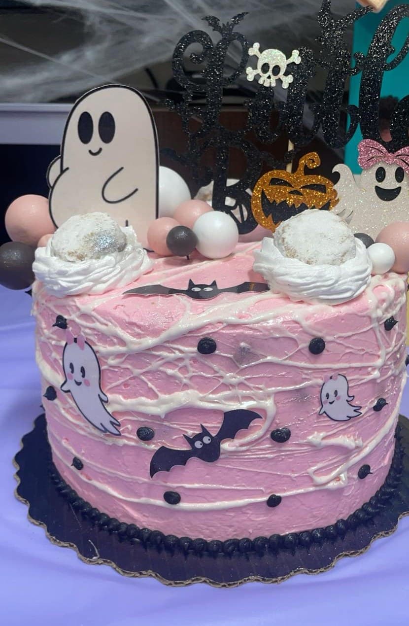 Pink Halloween cake decorated with friendly ghosts, bats and a white web drizzle.
